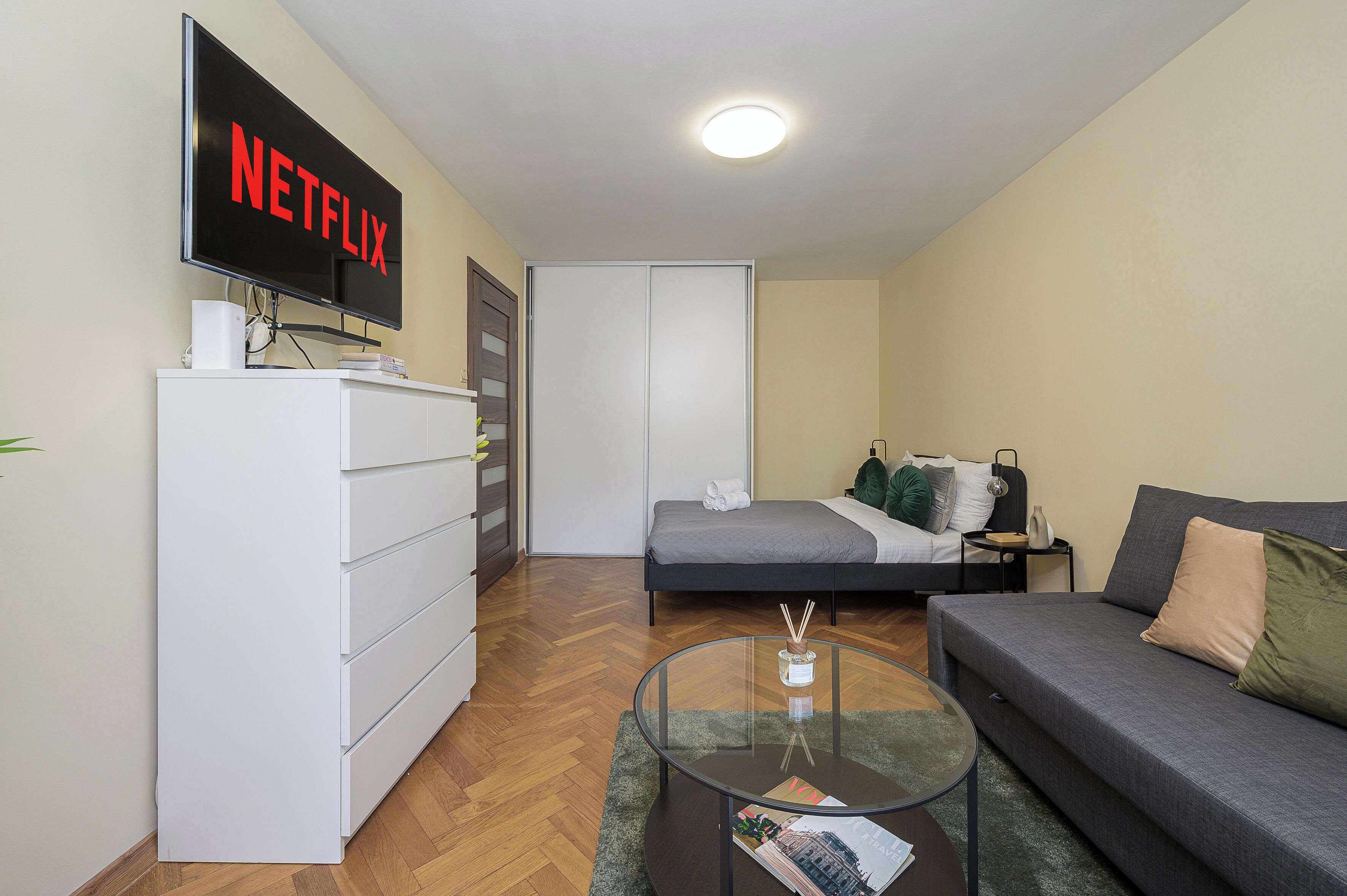 A modern bedroom with a bed, a sofa, a TV mounted on the wall, and a dresser.