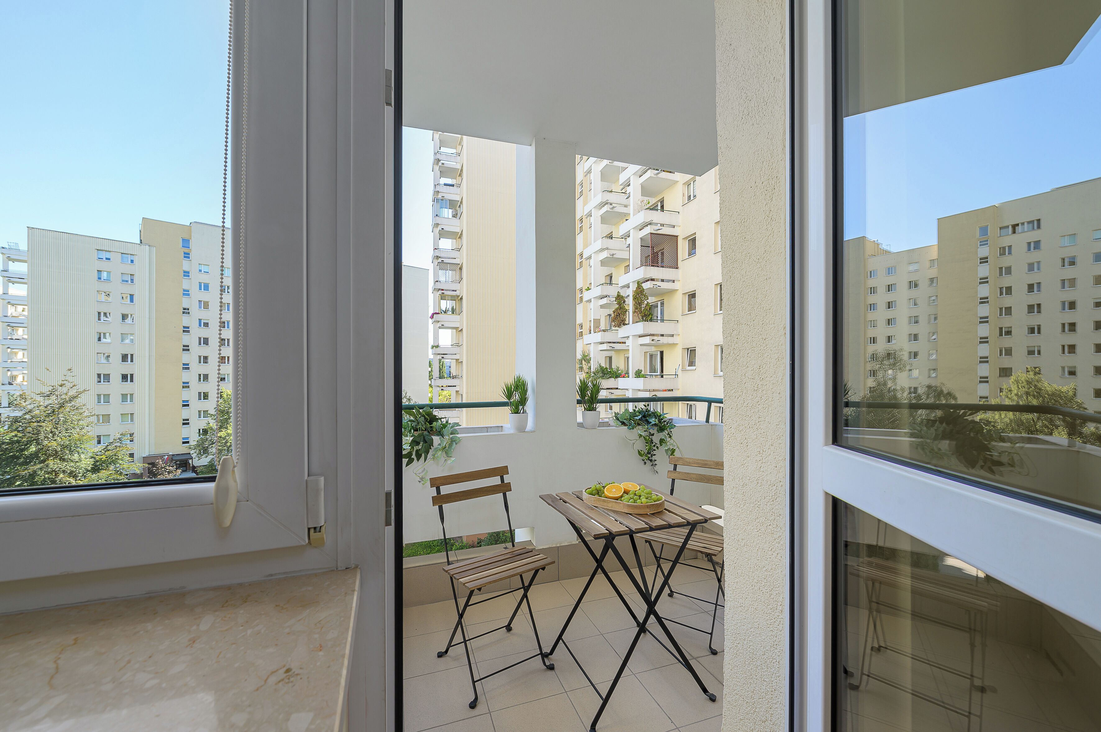 Varanda com mesa e cadeiras, um vaso de plantas e vista para edifícios próximos.