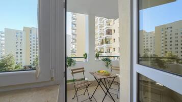 Varanda com mesa e cadeiras, um vaso de plantas e vista para edifícios próximos.
