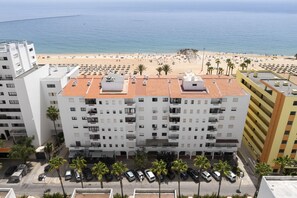 Ein mehrstöckiges Hotel mit Dachterrasse, Parkplatz und Blick auf einen Strand.