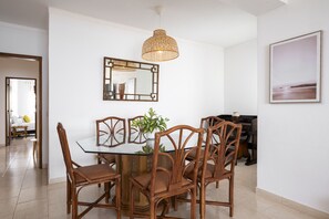 A dining area with a glass table surrounded by wicker chairs, a hanging wicker light fixture, a mirror, and a framed picture on the wall. - Gira Sol by Hdproperties (Quarteira)