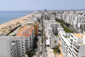 A coastal cityscape with high-rise buildings, a beach, and a clear sky. - Gira Sol by Hdproperties (Quarteira)