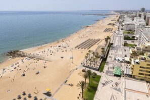 Eine Küstenstadt mit breitem Sandstrand, einer mit Palmen gesäumten Promenade und modernen Gebäuden.