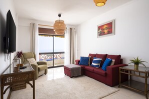 Ein modernes Wohnzimmer mit einem roten Sofa, einem Fernseher und einem Balkon mit Blick.