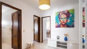 A hallway with a white console table, a blue vase with flowers, and a colorful abstract painting on the wall. - Gira Sol by Hdproperties (Quarteira)