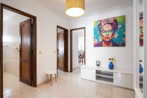 Ein Flur mit einem weißen Konsolentisch, einer blauen Vase mit Blumen und einem farbenfrohen, abstrakten Gemälde an der Wand.