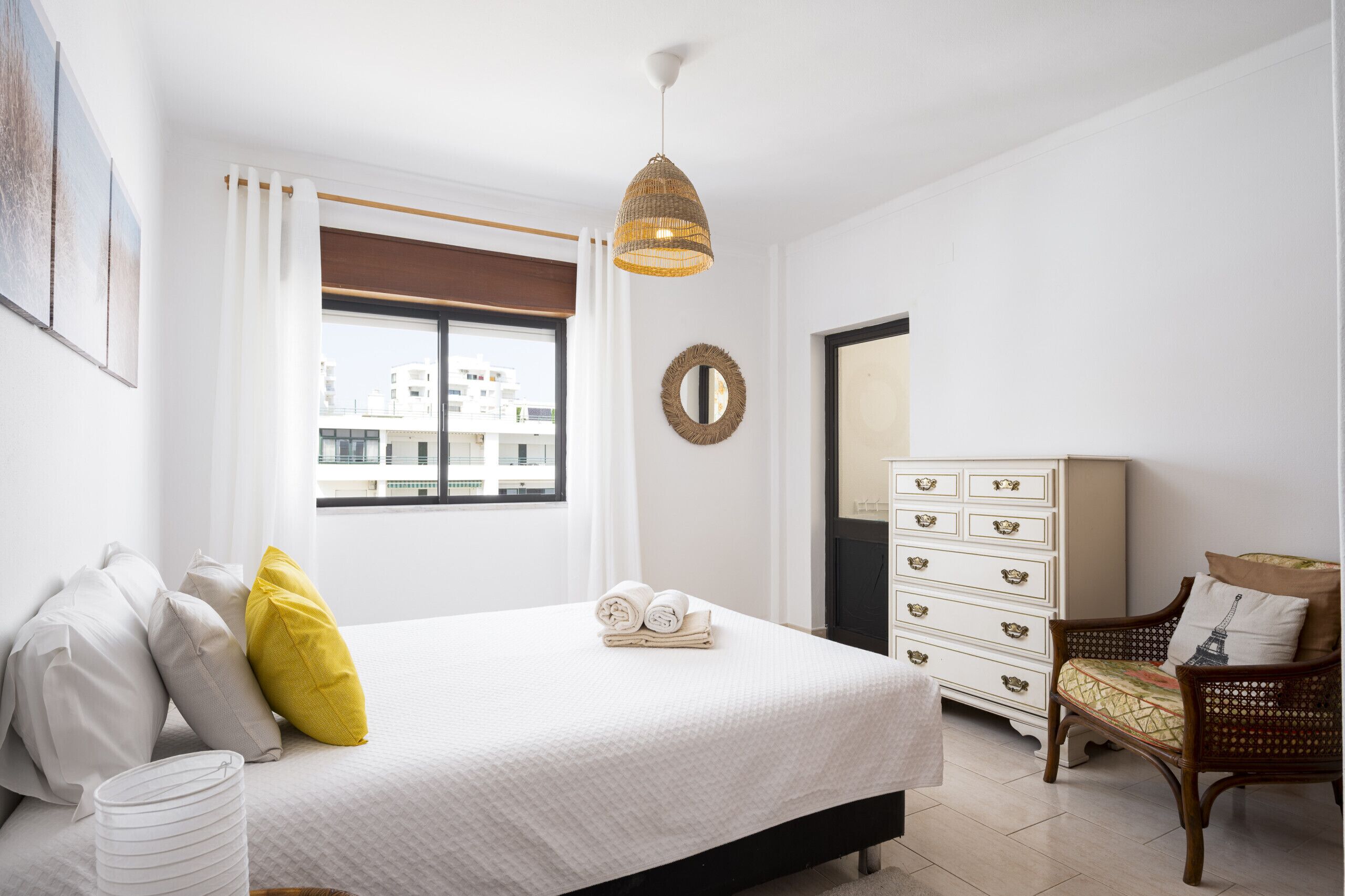 Une chambre à coucher comprenant un lit, une commode, une chaise, une fenêtre avec vue et un luminaire suspendu.