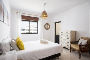 Un dormitorio con cama, cómoda, silla, ventana con vistas y lámpara colgante.