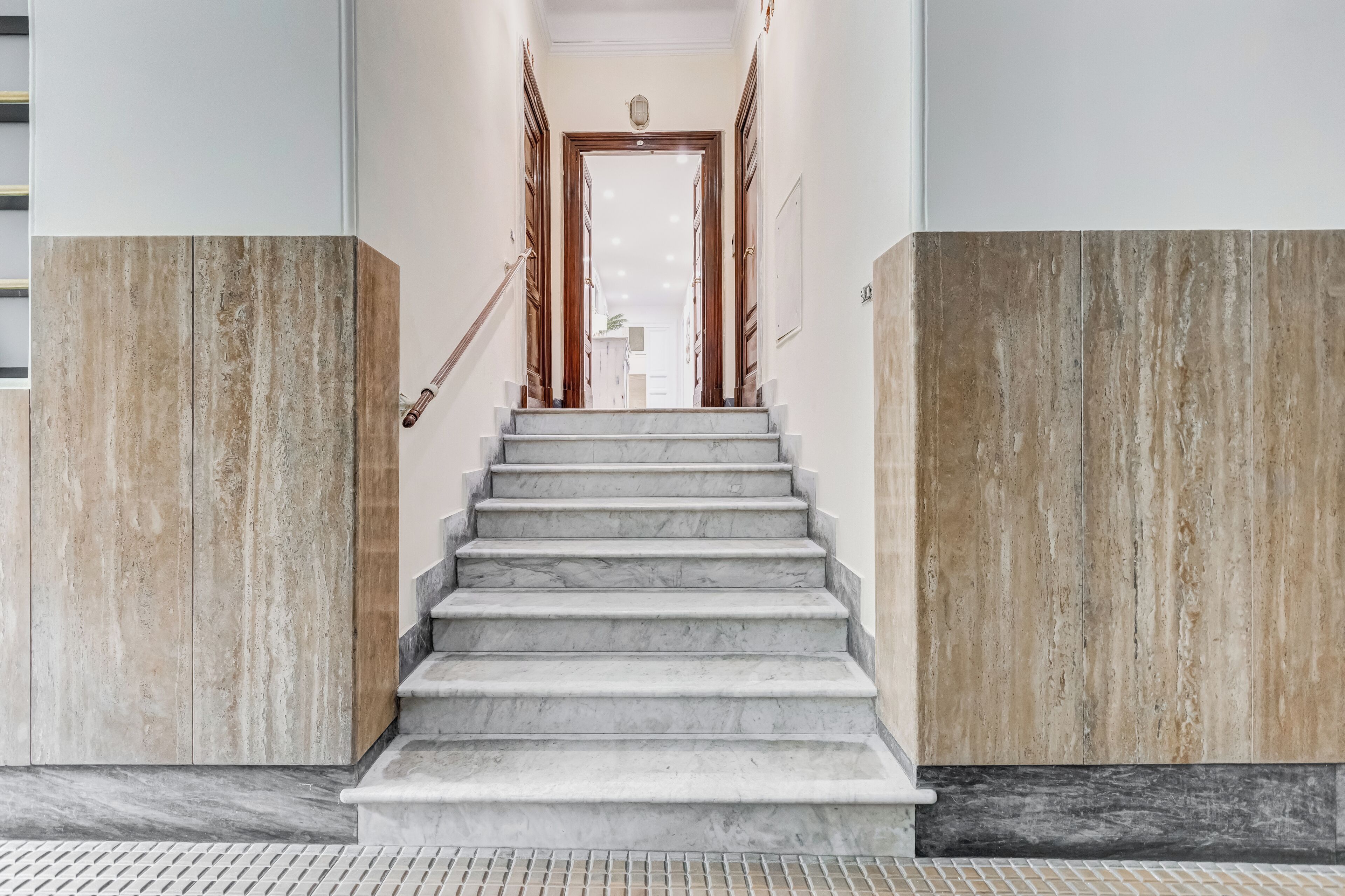 Una escalera de mármol que conduce a una puerta con una lámpara colgante encima.