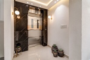 A modern elevator with a glass door, a marble wall, and a small potted plant on the floor. - Golden Key - Adarsh Nagar I Near Maxx & Fortis Hospital (New Delhi)