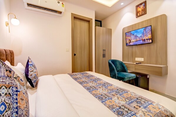 A hotel room with a bed, a desk, a chair, a television, and a wardrobe.