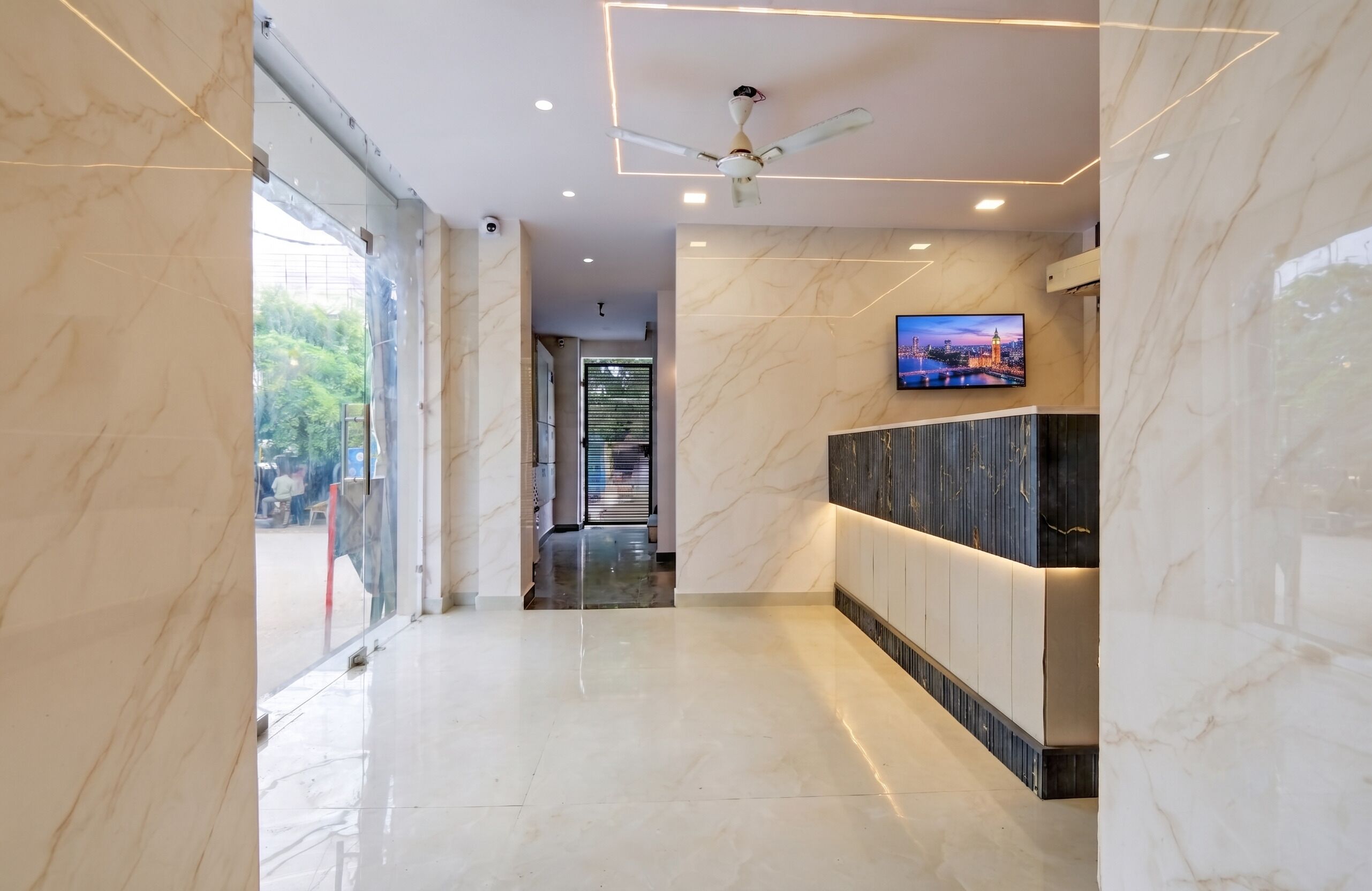 A modern hallway with marble flooring, a ceiling fan, recessed lighting, and a television mounted on the wall.