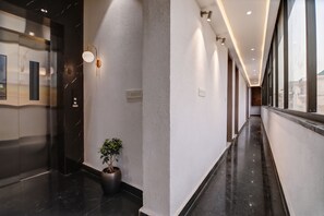 A modern hallway with a marble floor, a potted plant, and a wall-mounted light fixture.