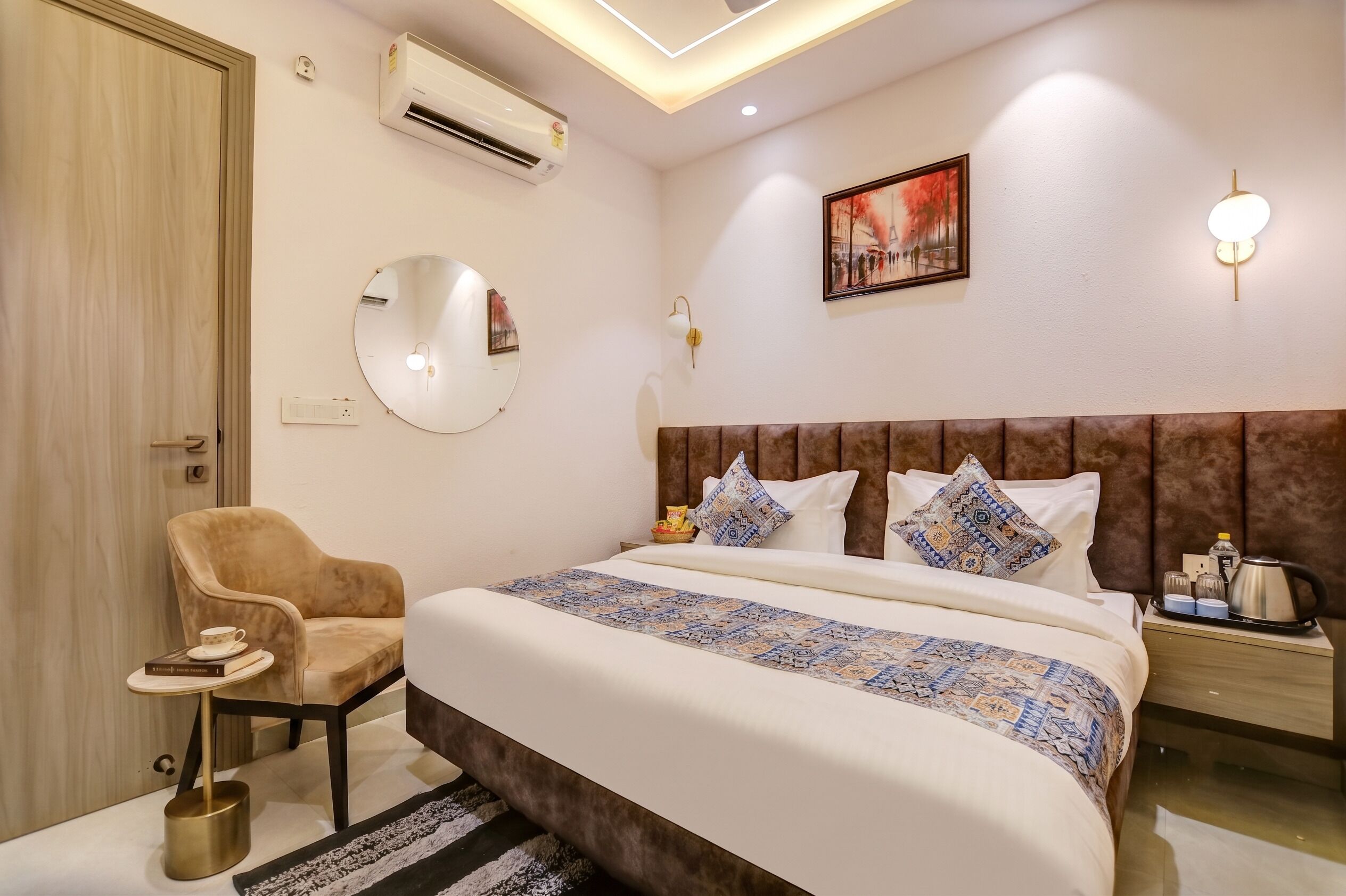 Ein Hotelzimmer mit Bett, Sessel, Nachttisch, Lampe und Klimaanlage.