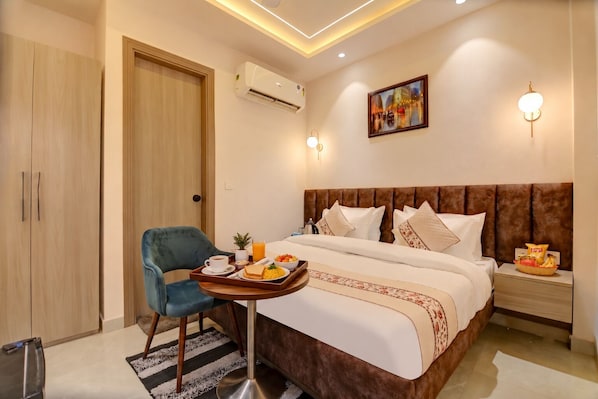 A hotel room with a bed, a chair, a tray with breakfast items, an air conditioning unit, and a painting on the wall.