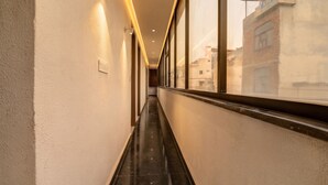 A corridor with a reflective floor, walls with recessed lighting, and a window with a view of buildings. - Golden Key - Adarsh Nagar I Near Maxx & Fortis Hospital (New Delhi)