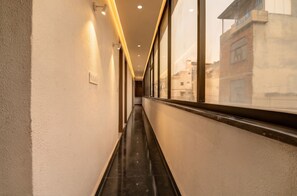 A corridor with a reflective floor, walls with recessed lighting, and a window with a view of buildings.