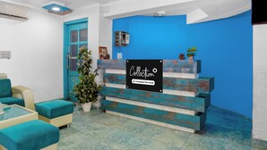 A reception desk with a sign, a blue wall, a door, and a seating area with cushions. - Super Collection O Queens  (Jaipur)
