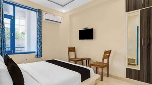 A hotel room with a bed, a TV, two chairs, a small table, and a wardrobe. - Super Collection O Queens  (Jaipur)