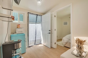 Una habitación compacta con kitchenette, una puerta que da a otra habitación y una pequeña mesa con un florero.