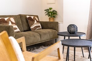 Ein Wohnzimmer mit einer Couch, zwei runden Tischen, einer Topfpflanze und einer Wandleuchte.