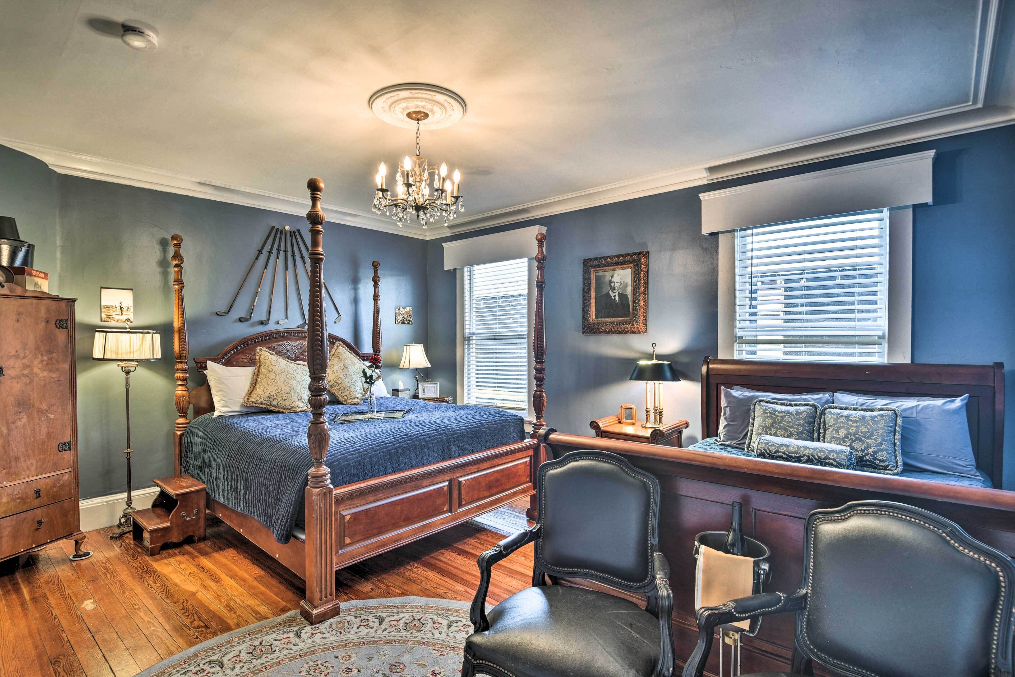A bedroom with a four-poster bed, a chandelier, a desk with a chair, and a dresser.
