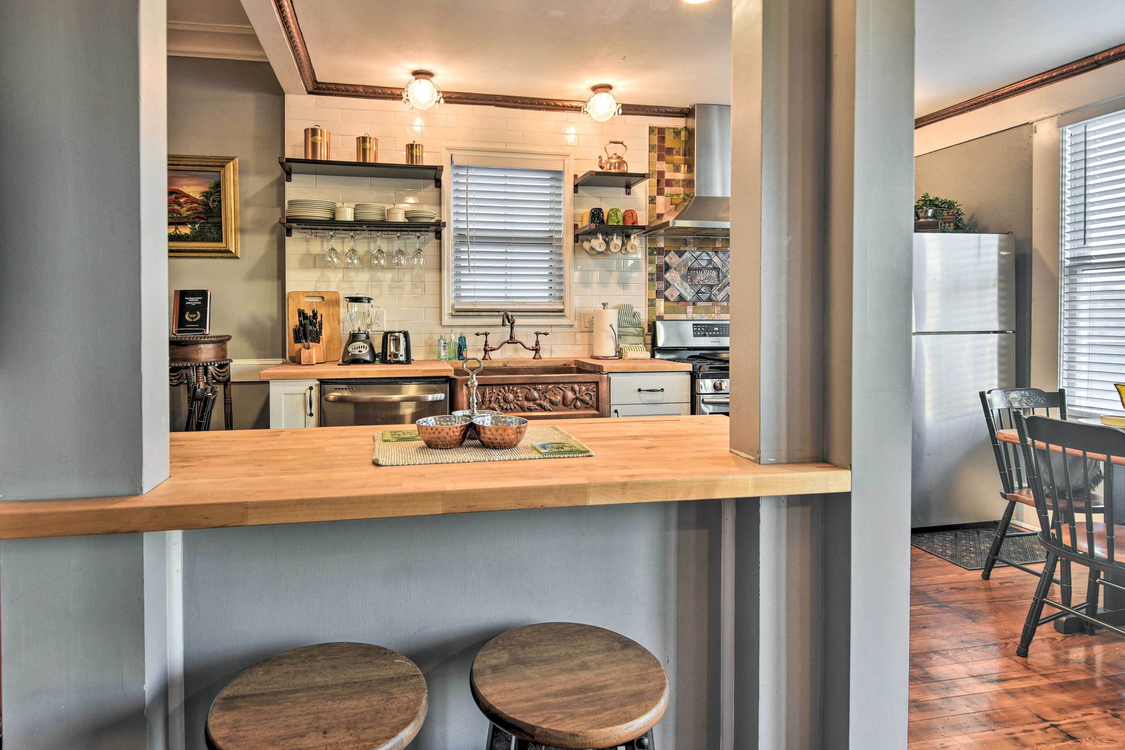 Une cuisine avec un plan de travail en bois, deux tabourets, un réfrigérateur et divers appareils de cuisine.