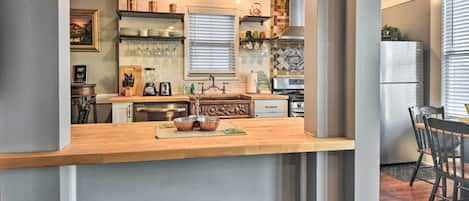A kitchen with a wooden countertop, two stools, a refrigerator, and various kitchen appliances.