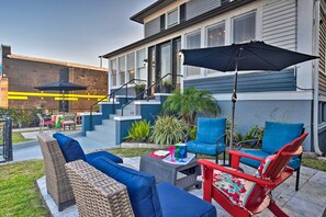 Eine Terrasse im Freien mit Korbmöbeln, einem roten Stuhl und einem schwarzen Sonnenschirm.