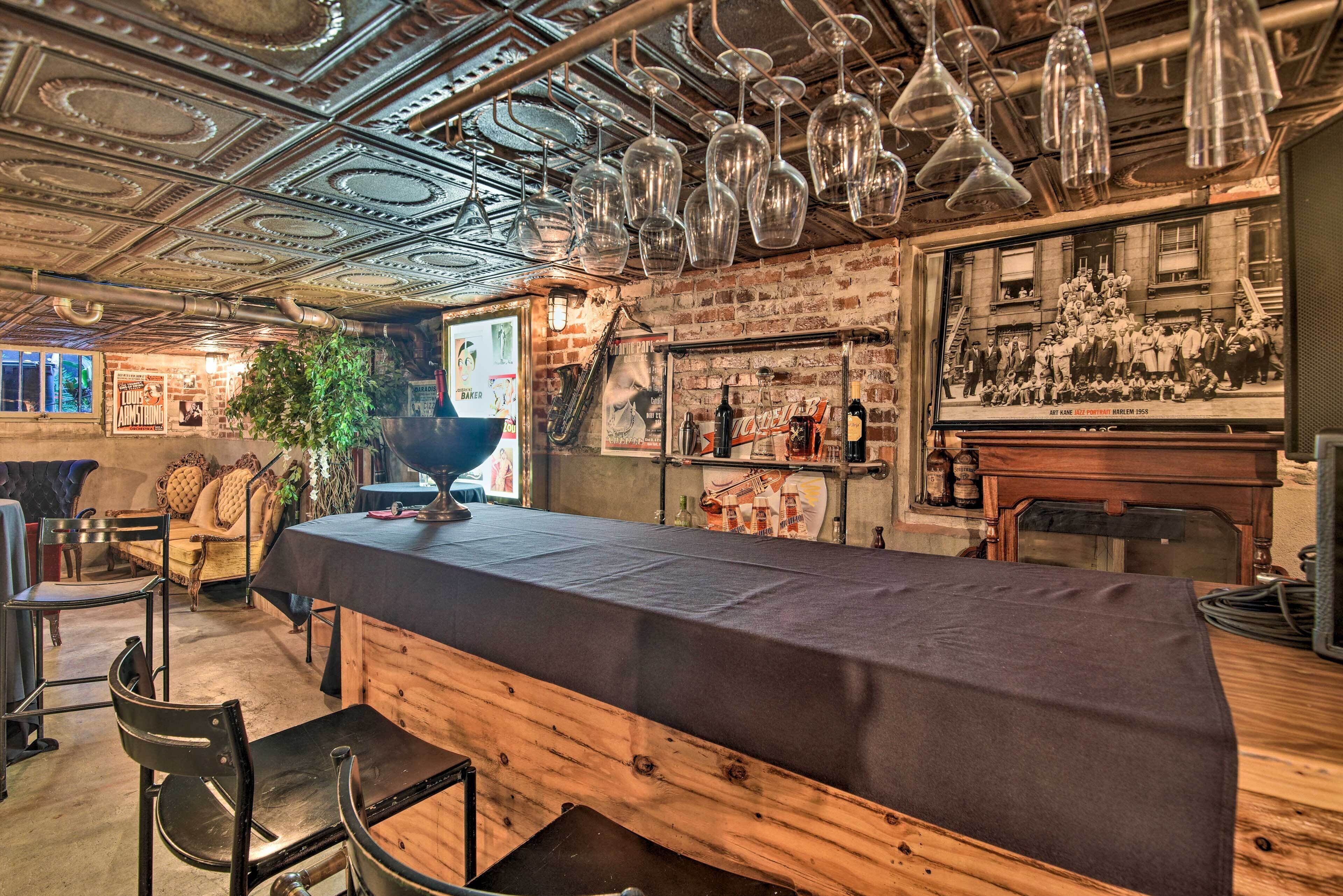 Uma área de bar com um balcão comprido, copos de vinho pendurados e um cartaz antigo na parede.
