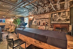 Uma área de bar com um balcão comprido, copos de vinho pendurados e um cartaz antigo na parede.