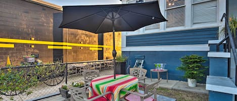Une terrasse extérieure avec une table et des chaises, un grand parasol et une plante en pot.