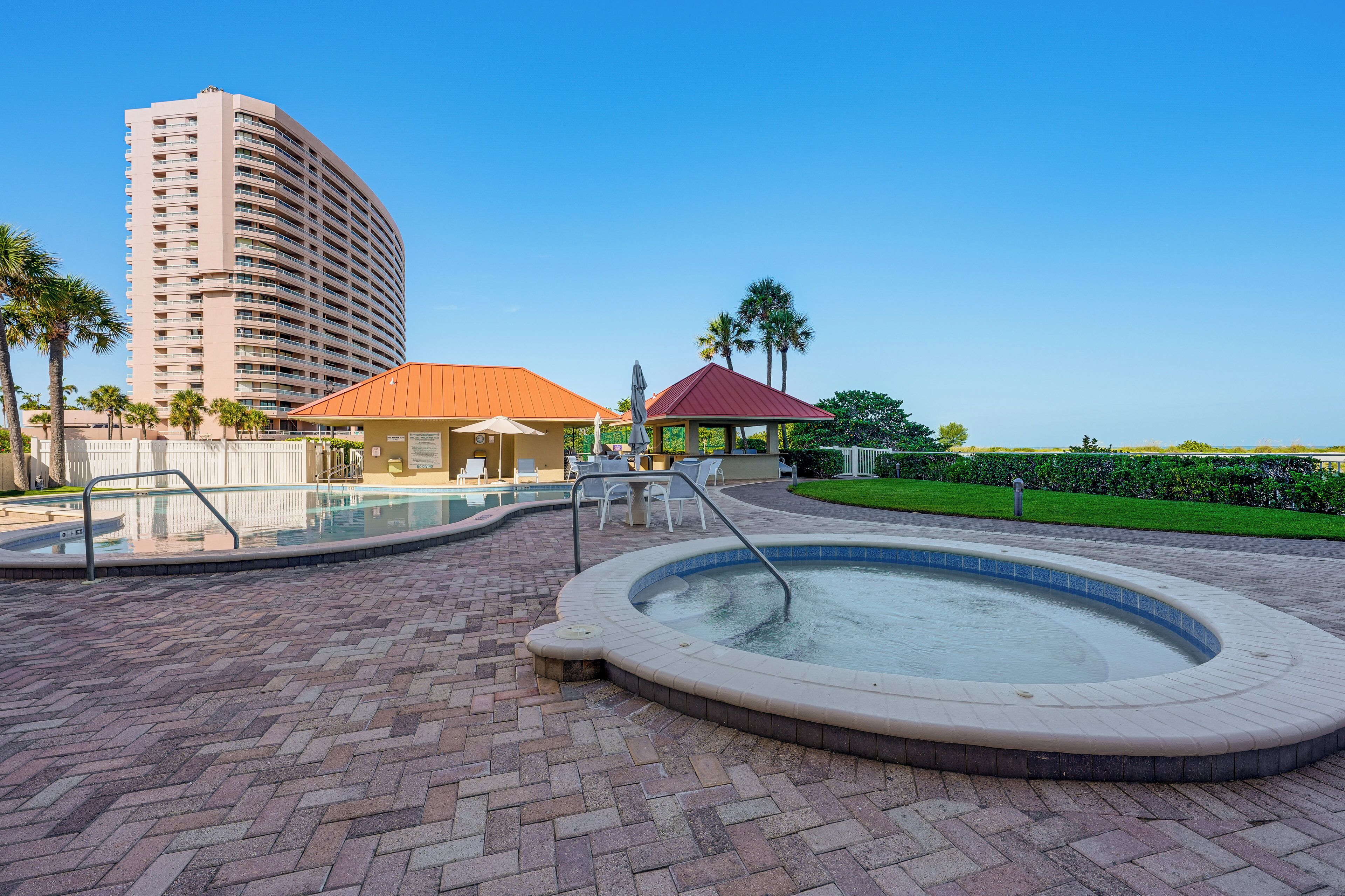 A hotel pool area with a hot tub, lounge chairs, and a building in the background.