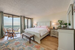 A bedroom with a bed, bedside tables, a bench, a chair, a balcony, and a view of the sea. - Majestic Gulf Views Condo w/ Balcony (Clearwater Beach)