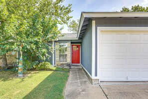 A residential garage with a red door, a stone wall, and a tree in the foreground. - Fenced Yard! Austin Group Escape Near Golf (Austin)