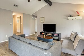 A modern living room with a sectional sofa, a coffee table, a flat-screen TV, and a bookshelf. - Fenced Yard! Austin Group Escape Near Golf (Austin)