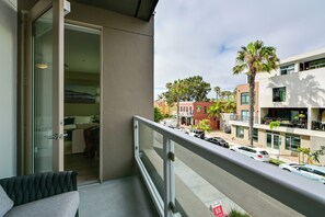 A balcony with a view of a street, a building with a sign, and parked cars. - Steps to the Sand! Luxury Oceanside Pier Condo (Oceanside)