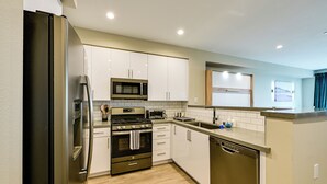 A modern kitchen with stainless steel appliances, white cabinetry, and a wooden floor. - Steps to the Sand! Luxury Oceanside Pier Condo (Oceanside)