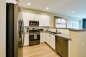 A modern kitchen with stainless steel appliances, white cabinetry, and a wooden floor. - Steps to the Sand! Luxury Oceanside Pier Condo (Oceanside)