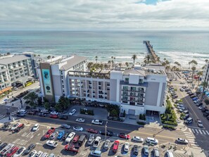 A hotel with multiple floors, a parking lot, and a view of the ocean. - Steps to the Sand! Luxury Oceanside Pier Condo (Oceanside)