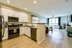 A modern kitchen with stainless steel appliances, a dishwasher, and a dining area with a sofa and table. - Steps to the Sand! Luxury Oceanside Pier Condo (Oceanside)