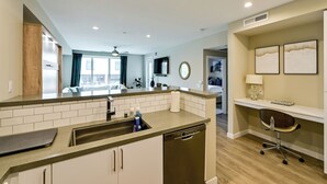 A modern kitchen with a dishwasher, a sink, and a countertop. There is a dining area with a table and chairs visible in the background. - Steps to the Sand! Luxury Oceanside Pier Condo (Oceanside)