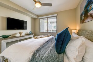 A hotel room with a bed, a flat-screen TV, a window, and a ceiling fan. - Steps to the Sand! Luxury Oceanside Pier Condo (Oceanside)