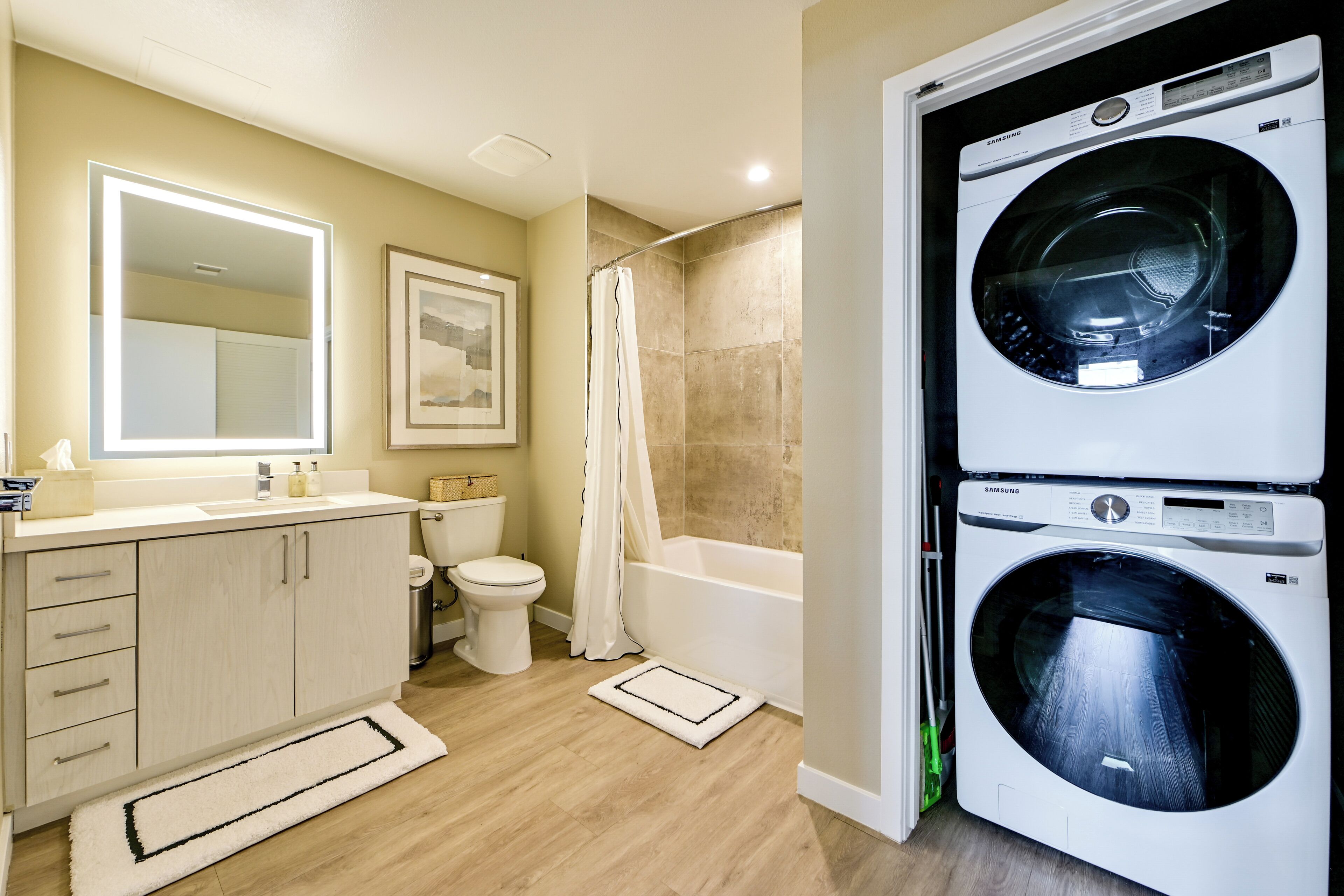 Une salle de bain moderne équipée de toilettes, d’un lavabo, d’un miroir et d’un lave-linge à double porte.