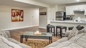 Ein modernes Wohnzimmer mit einem Glastisch, Holzboden und einer Couch mit gemusterten Kissen.