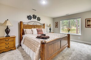 A bedroom with a wooden bed, two bedside tables with lamps, a window with a view, and a wall with decorative elements. - Luxury Forest Retreat: Movie Room, Games, Hot Tub (Colorado Springs)