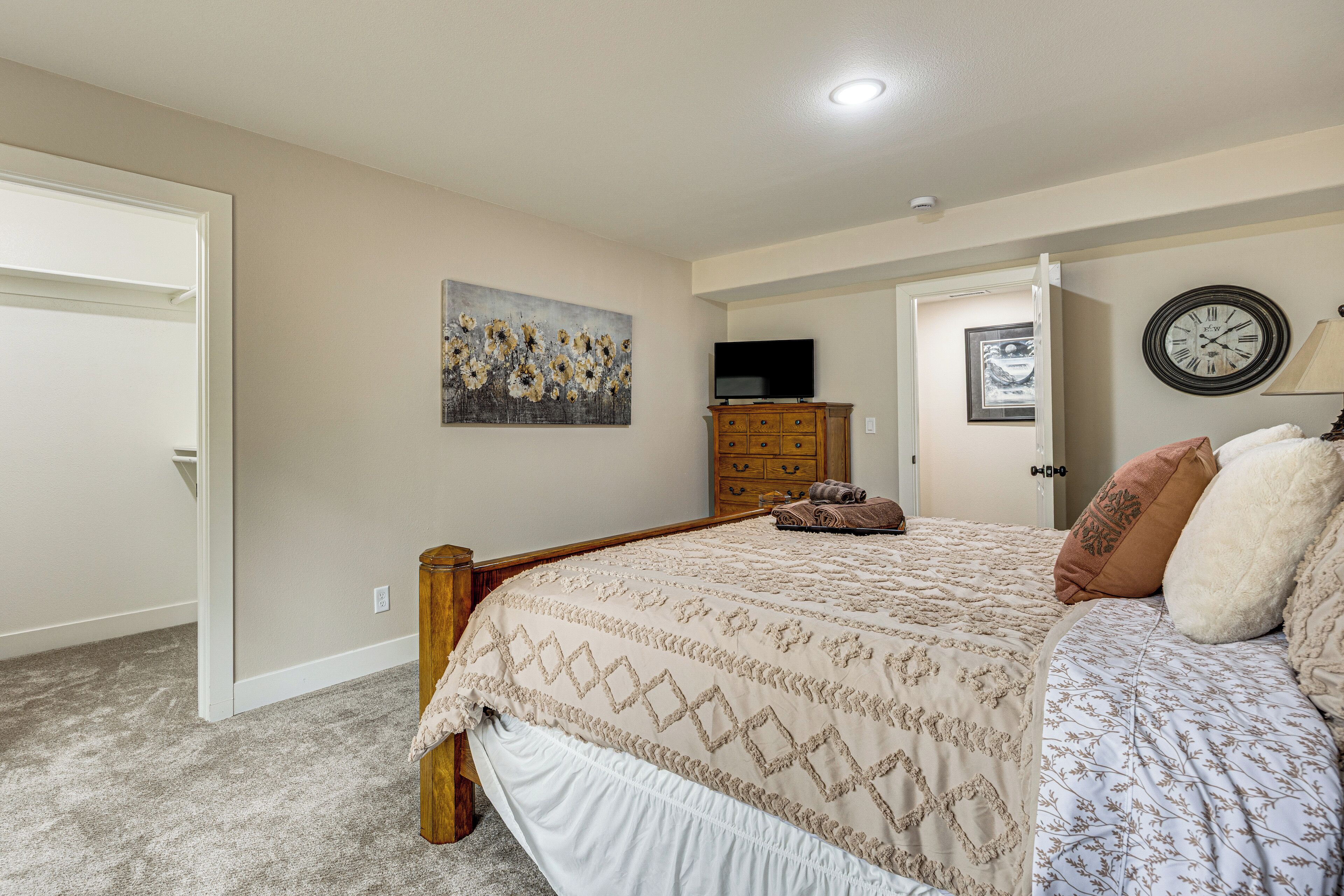A bedroom with a bed, a dresser, a painting, a clock, and a door.