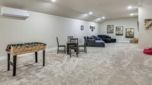 Ein Zimmer mit einem Kicker, einem Esstisch mit Stühlen, einer Couch und mehreren Bildern an der Wand.