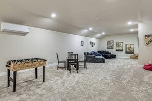 Ein Zimmer mit einem Kicker, einem Esstisch mit Stühlen, einer Couch und mehreren Bildern an der Wand.