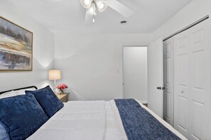 A bedroom with a bed, a nightstand with a lamp, a painting on the wall, and a door. - Golf & Chill! Family-friendly Augusta Home (Augusta)